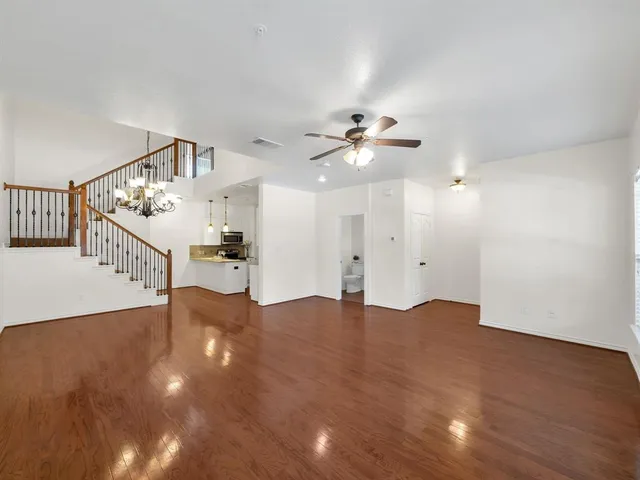 a view of an empty room with chandelier fan and wooden floor