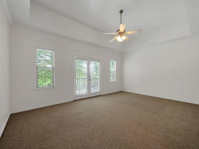 an empty room with chandelier fan and windows