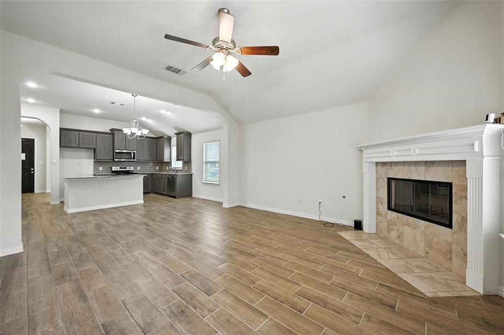 5 Pheasant Run Sanger, TX 76266 - Photo 18 of 27 Unfurnished living room with a chandelier, lofted ceiling, a tile fireplace, wood finish floors, and a ceiling fan
