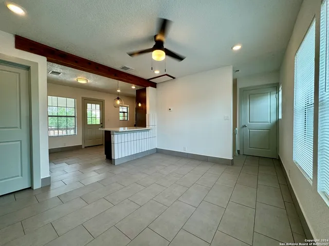 an empty room with kitchen view and a chandelier fan
