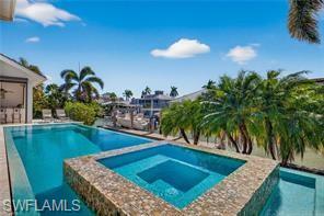 1330 Marlin Drive Naples, FL 34102 - Photo 43 of 44 Waterfront property featuring an outdoor swimming pool, integrated spa with mosaic tile surround, and lush palm trees