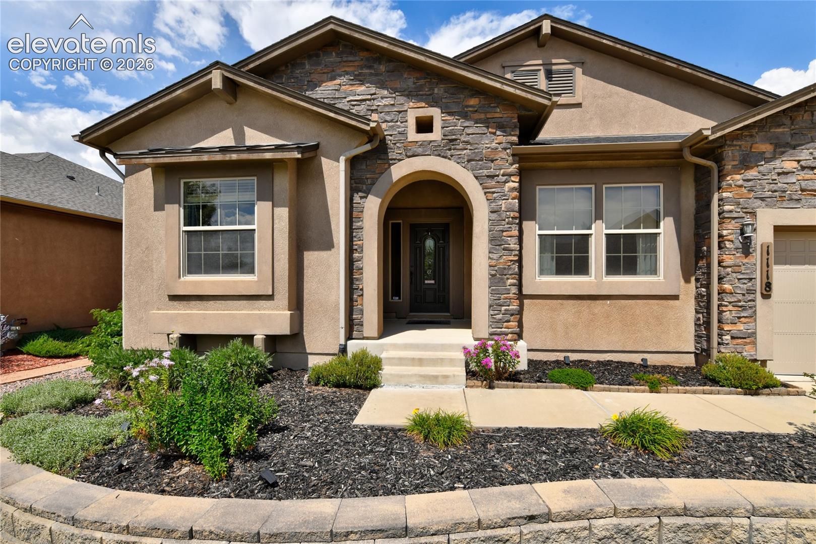 1118 Spectrum Loop Colorado Springs, CO 80921 - Photo 4 of 50 Stucco and stone facade with an arched entry, concrete steps, and integrated landscaping with retaining wall