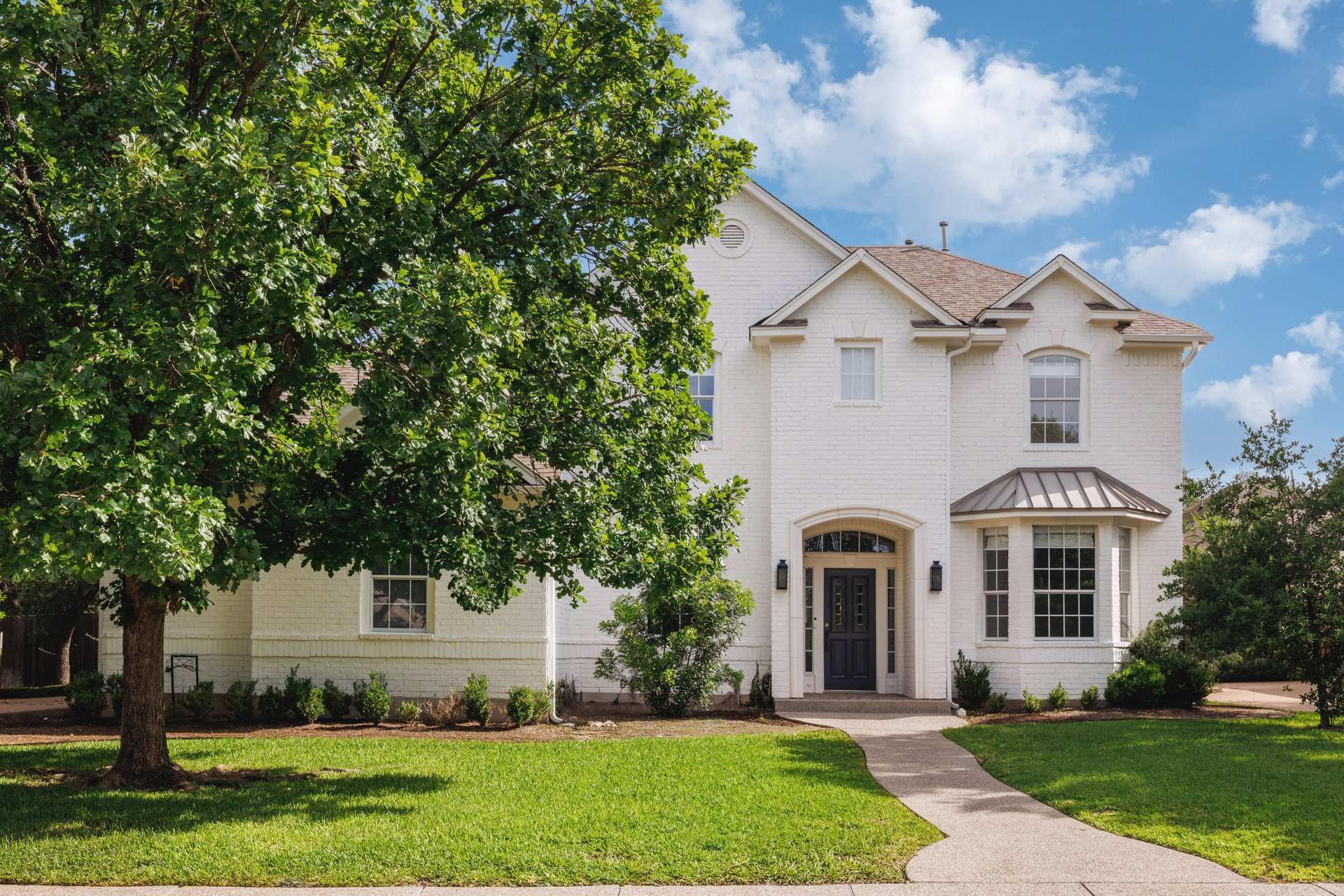 5512 Ballenton Lane Austin, TX 78739 - Photo 2 of 40 White brick home featuring a gracefully arched entryway and bay window, set amidst mature trees and a verdant lawn.