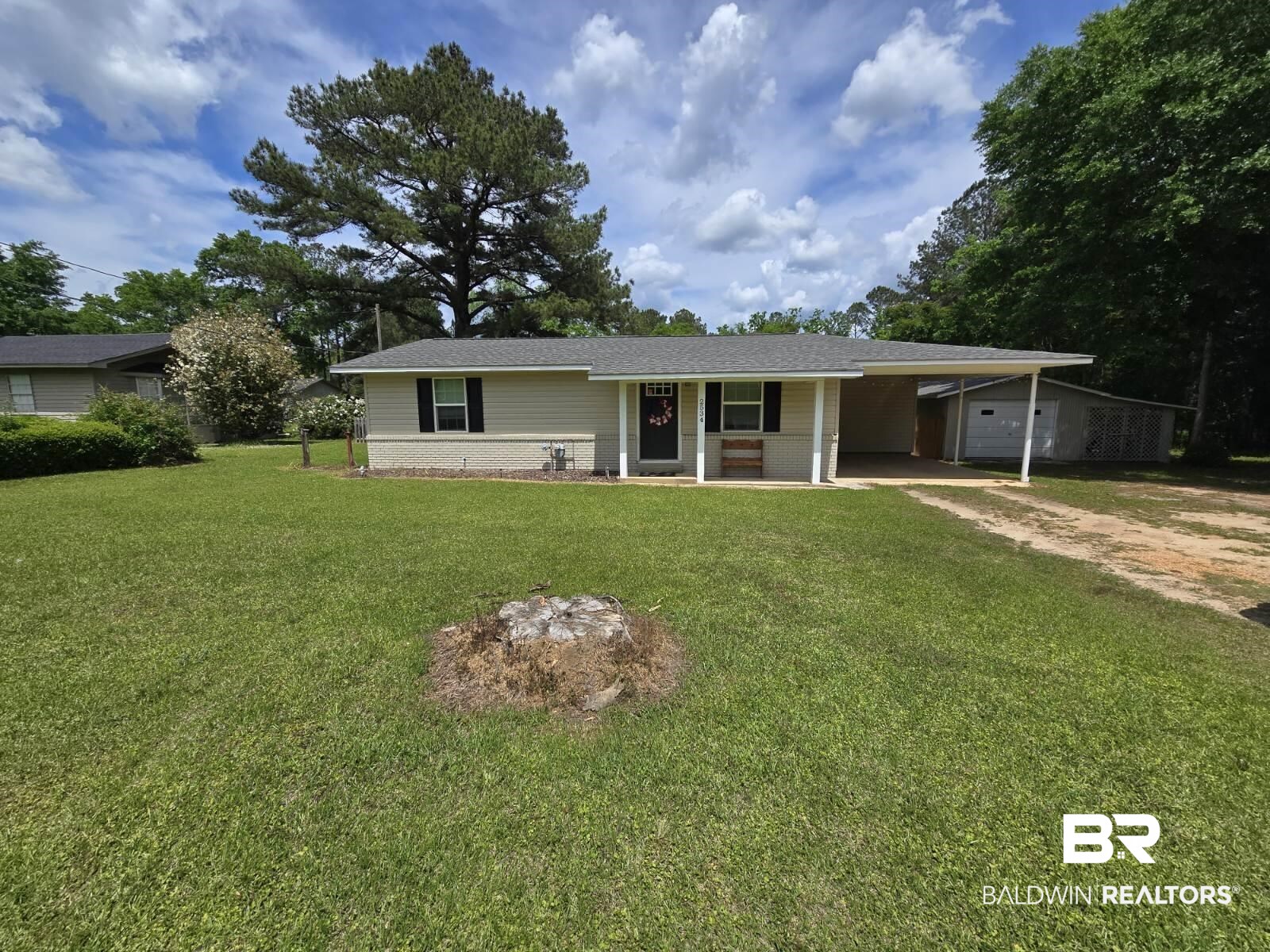 Ranch-style house featuring dirt driveway, a front yard, and an attached carport