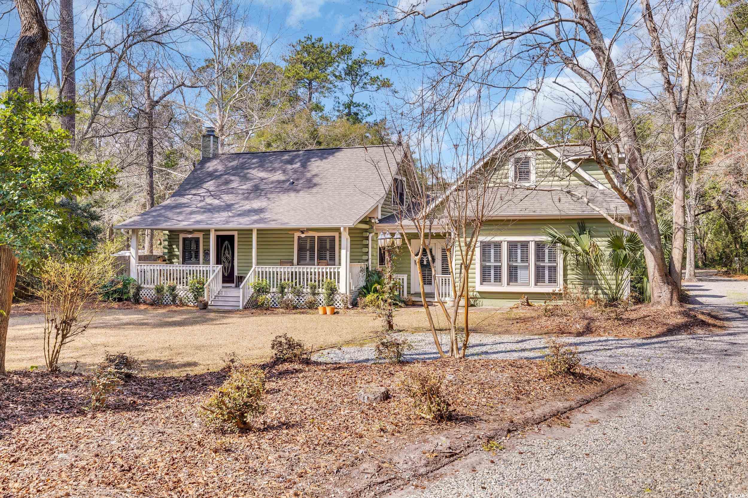 View of front facade with covered porch, driveway, and a chimney