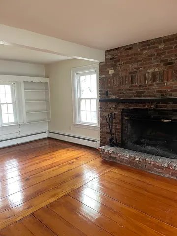 an empty room with wooden floor fireplace and windows