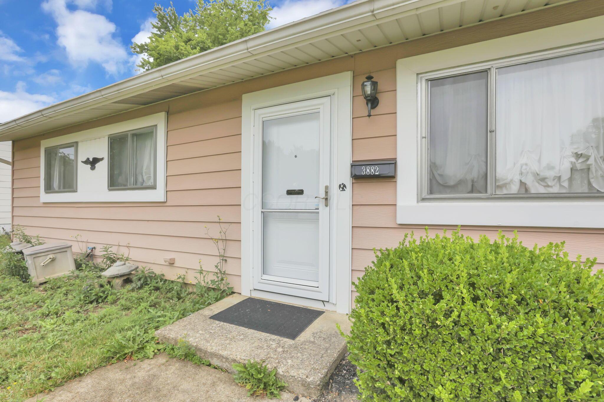 3882 Glenfield Road Columbus, OH 43232 - Photo 5 of 29 Pink siding exterior featuring white trim windows, an entry door with a screen door, and a street number plaque
