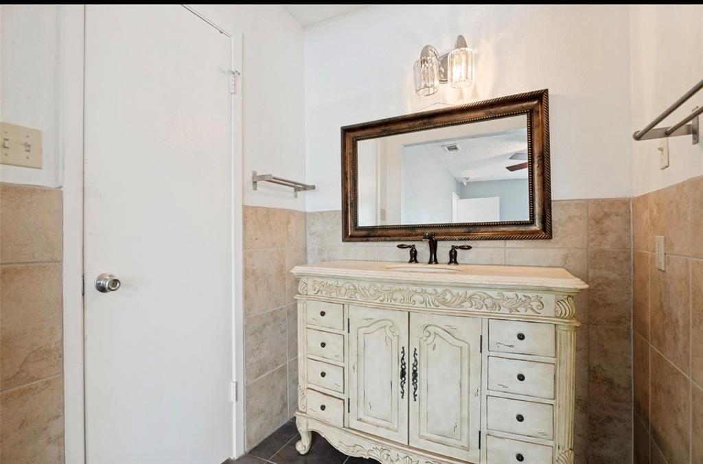 5808 Harvest Hill Road Dallas, TX 75230 - Photo 13 of 18 Bathroom featuring a carved vanity with a countertop, a framed mirror, and wall-mounted lighting