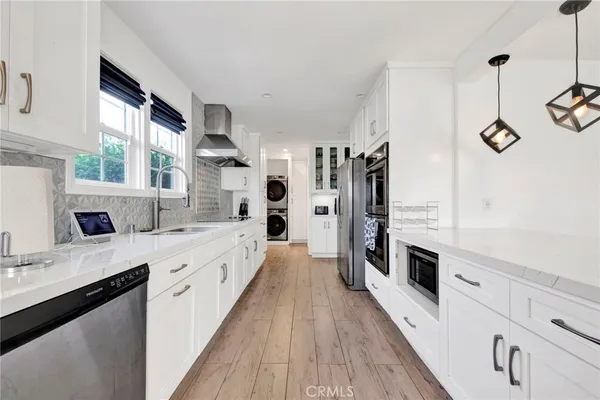 a large kitchen with stainless steel appliances a sink dishwasher a refrigerator and a stove with wooden floor