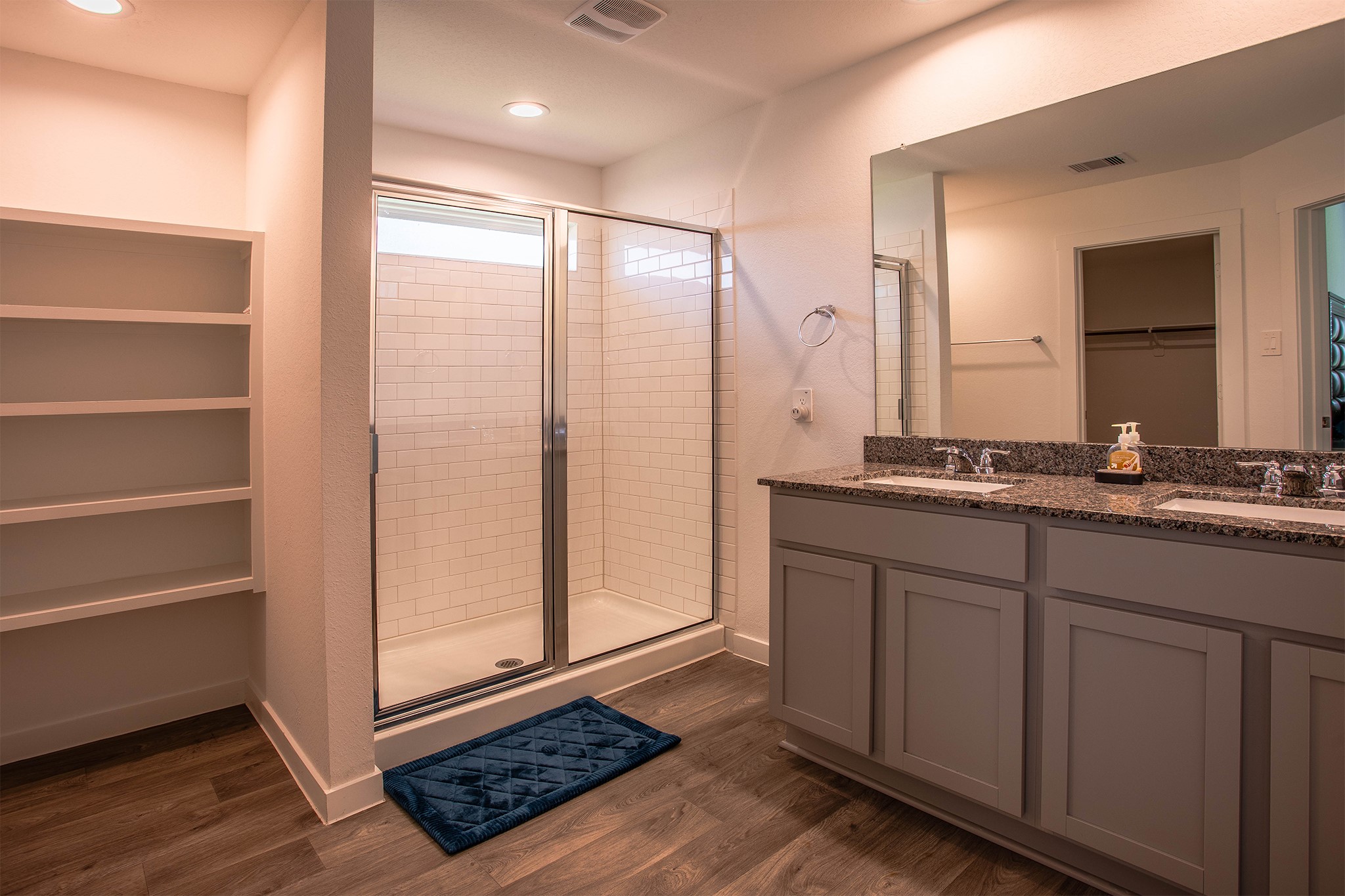 31810 Whittis Hill Way Fulshear, TX 77441 - Photo 10 of 23 The primary bathroom boasts a spacious and modern design featuring a large glass-enclosed shower with classic white subway tile, a dual-sink vanity with granite countertops, built-in shelving for storage, and direct access to your walk-in closet for added convenience.