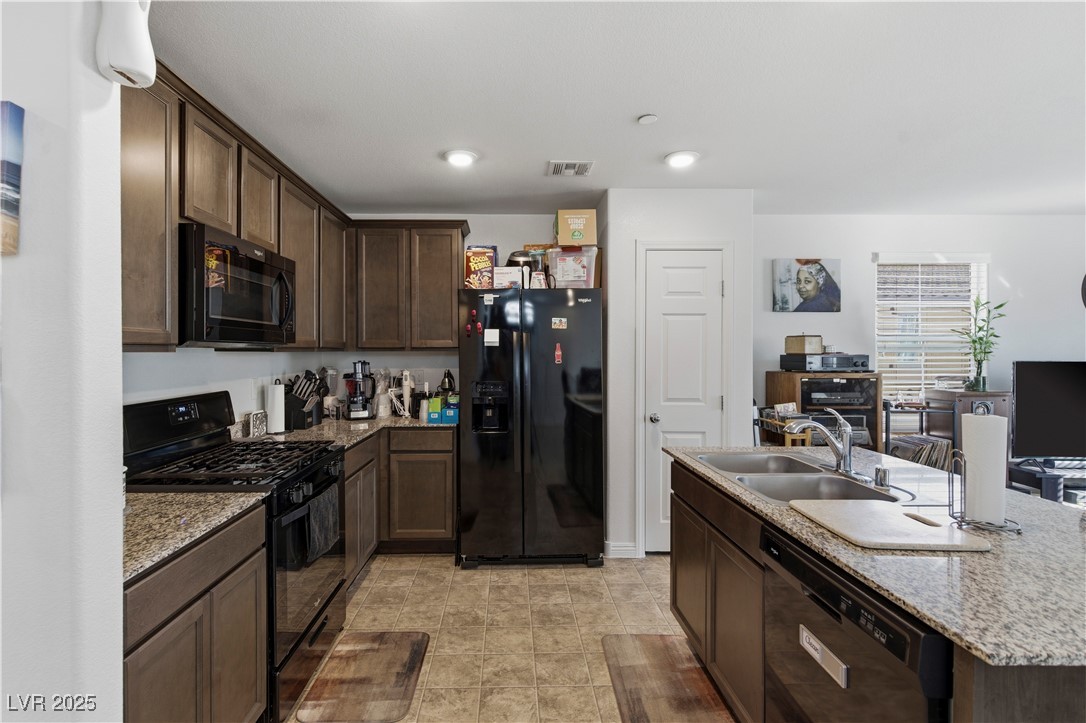 4648 Woolcomber Street Las Vegas, NV 89115 - Photo 10 of 41 Kitchen featuring dark brown cabinets, black appliances, light stone countertops, a center island with sink, and recessed lighting