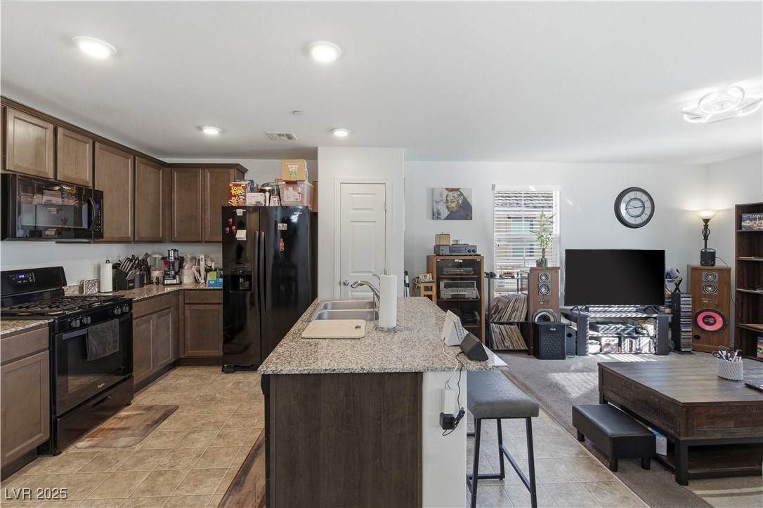 4648 Woolcomber Street Las Vegas, NV 89115 - Photo 40 of 41 Kitchen featuring black appliances, open floor plan, dark brown cabinetry, a breakfast bar, and light stone counters