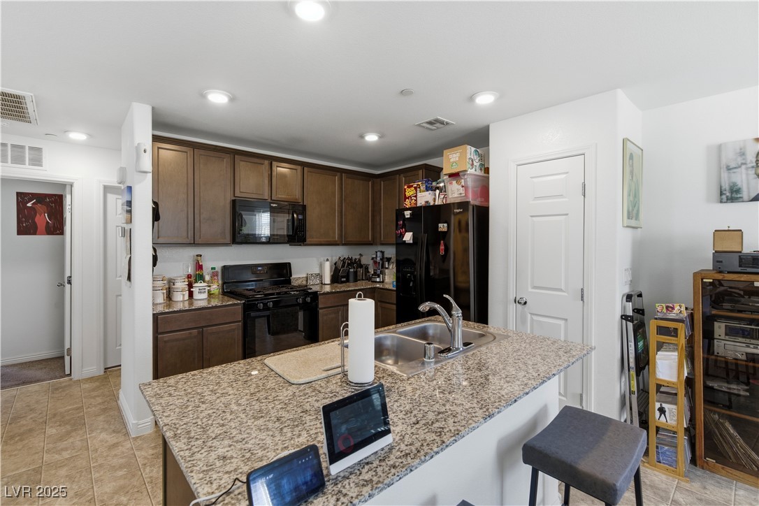 4648 Woolcomber Street Las Vegas, NV 89115 - Photo 11 of 41 Kitchen featuring black appliances, a kitchen bar, dark brown cabinets, an island with sink, and light tile patterned floors