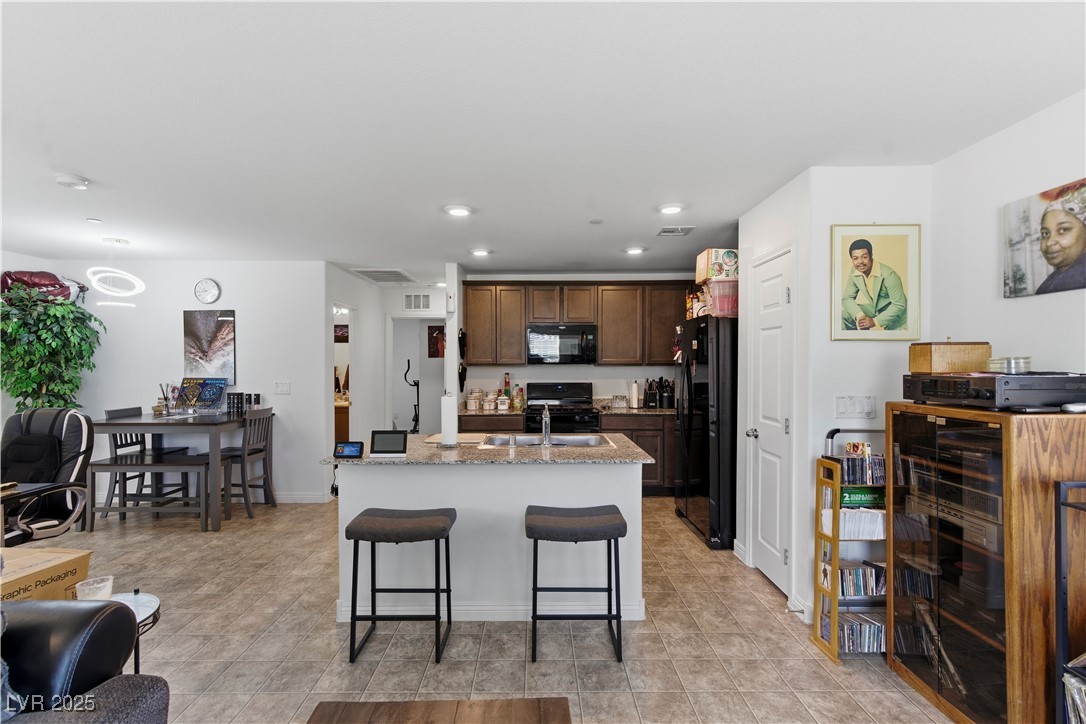 4648 Woolcomber Street Las Vegas, NV 89115 - Photo 12 of 41 Kitchen featuring an island with sink, a breakfast bar, recessed lighting, black appliances, and light stone countertops
