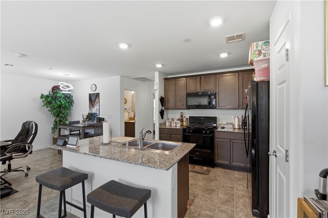 4648 Woolcomber Street Las Vegas, NV 89115 - Photo 13 of 41 Kitchen featuring an office area, black appliances, a breakfast bar, light stone counters, and an island with sink