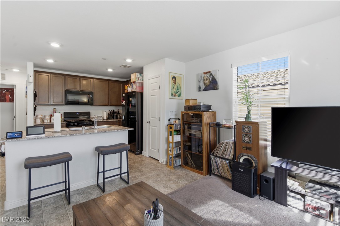 4648 Woolcomber Street Las Vegas, NV 89115 - Photo 17 of 41 Kitchen featuring a kitchen breakfast bar, black appliances, light stone countertops, dark brown cabinets, and recessed lighting