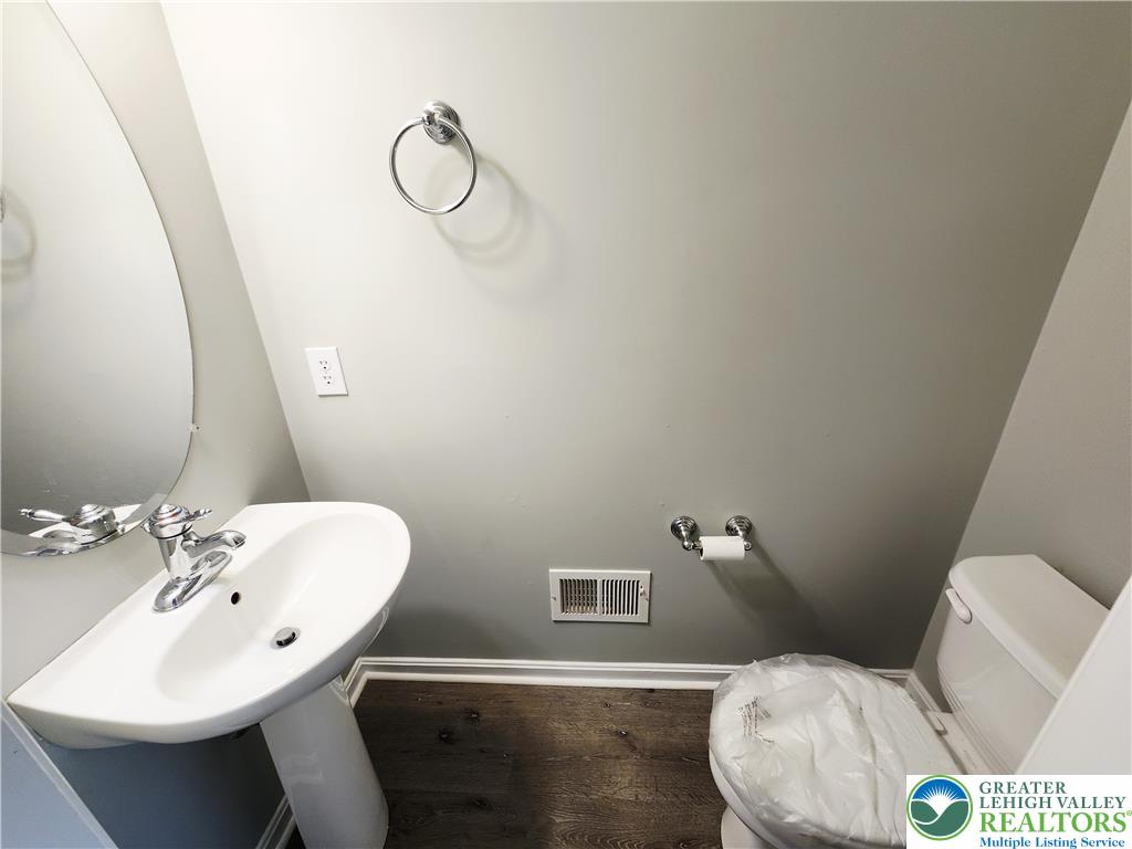 8513 Gateway Road Breinigsville, PA 18031 - Photo 18 of 45 A compact and functional bathroom showcasing a pedestal sink, toilet, and rich hardwood flooring.