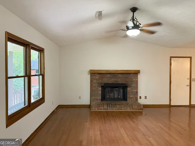 a view of an empty room with wooden floor fireplace and a window