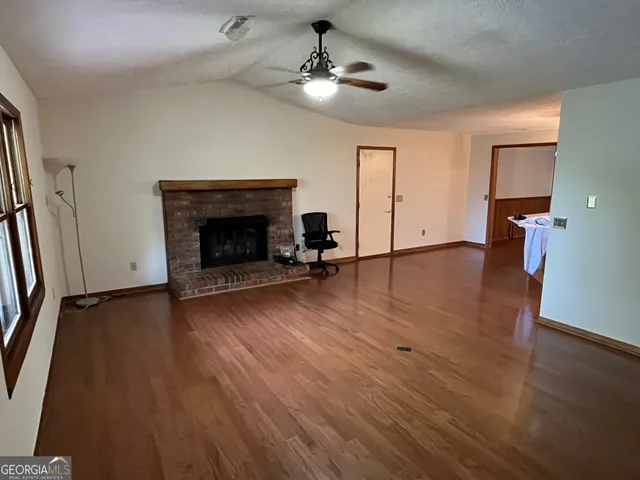 an empty room with wooden floor a fireplace a ceiling fan and windows