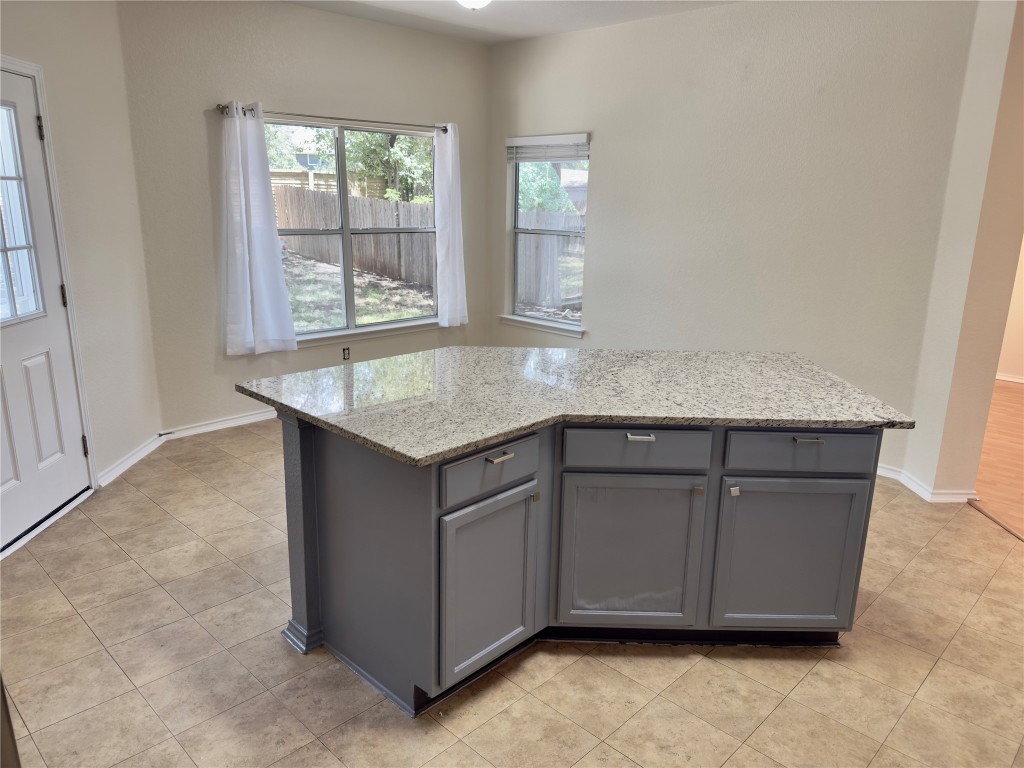 1206 Devil Ridge Cedar Park, TX 78613 - Photo 8 of 38 Kitchen with gray cabinets, light stone counters, light tile patterned floors, and a kitchen island