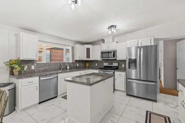 a kitchen with granite countertop a refrigerator sink and white cabinets