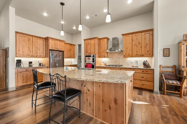 a kitchen with stainless steel appliances kitchen island granite countertop a stove a refrigerator and wooden cabinets with wooden floor