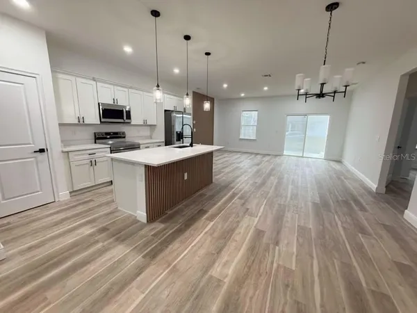 a open kitchen with kitchen island a stove a sink dishwasher a refrigerator white cabinets and wooden floor next to a window