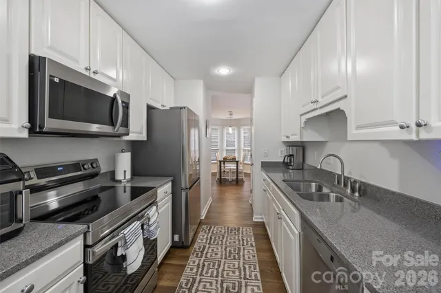 a kitchen with stainless steel appliances granite countertop a sink a stove oven a refrigerator with grey cabinets and wooden floor