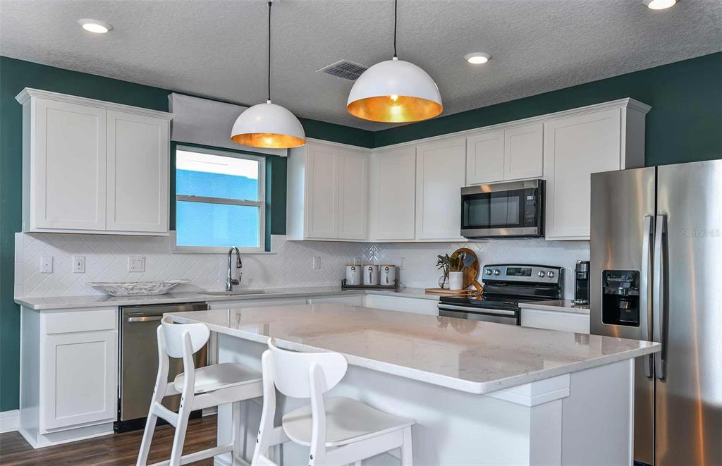 12816 Blue Reflection Avenue Parrish, FL 34219 - Photo 3 of 12 a kitchen with stainless steel appliances granite countertop a sink a stove a microwave a refrigerator cabinets and chairs