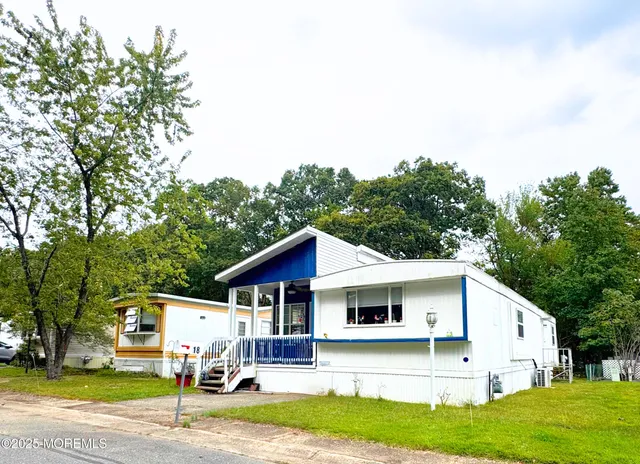 a view of a white house with a big yard plants and large trees