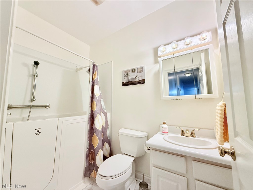 603 South Raccoon Road, Unit 1 Austintown, OH 44515 - Photo 18 of 22 Bathroom featuring a walk-in tub with grab bar and handheld shower, a white vanity with an integrated sink, a medicine cabinet with a four-bulb light fixture, and a standard toilet