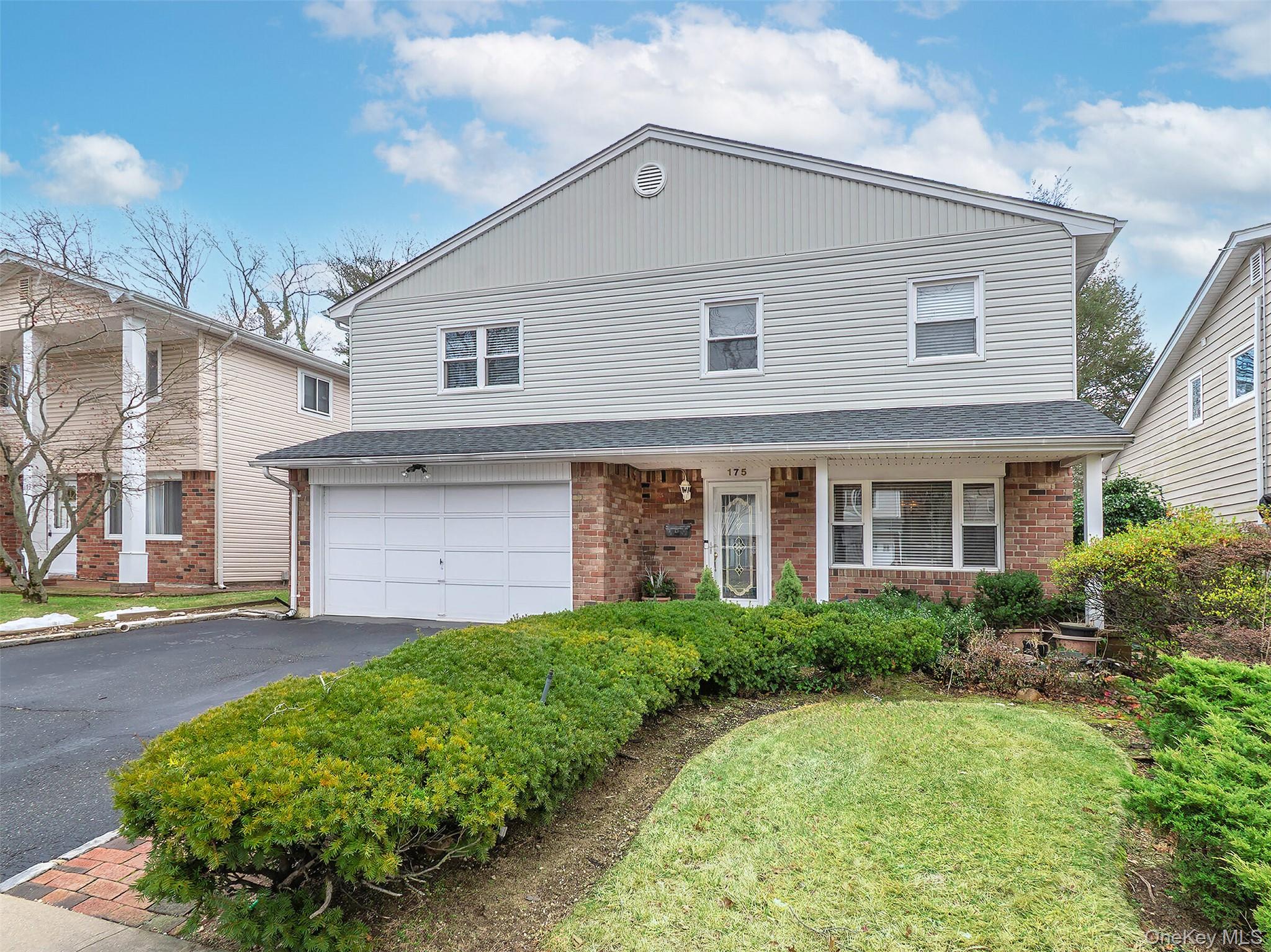 175 Soundview Drive Port Washington, NY 11050 - Photo 1 of 1 Traditional home featuring a porch, driveway, brick siding, a shingled roof, and an attached garage