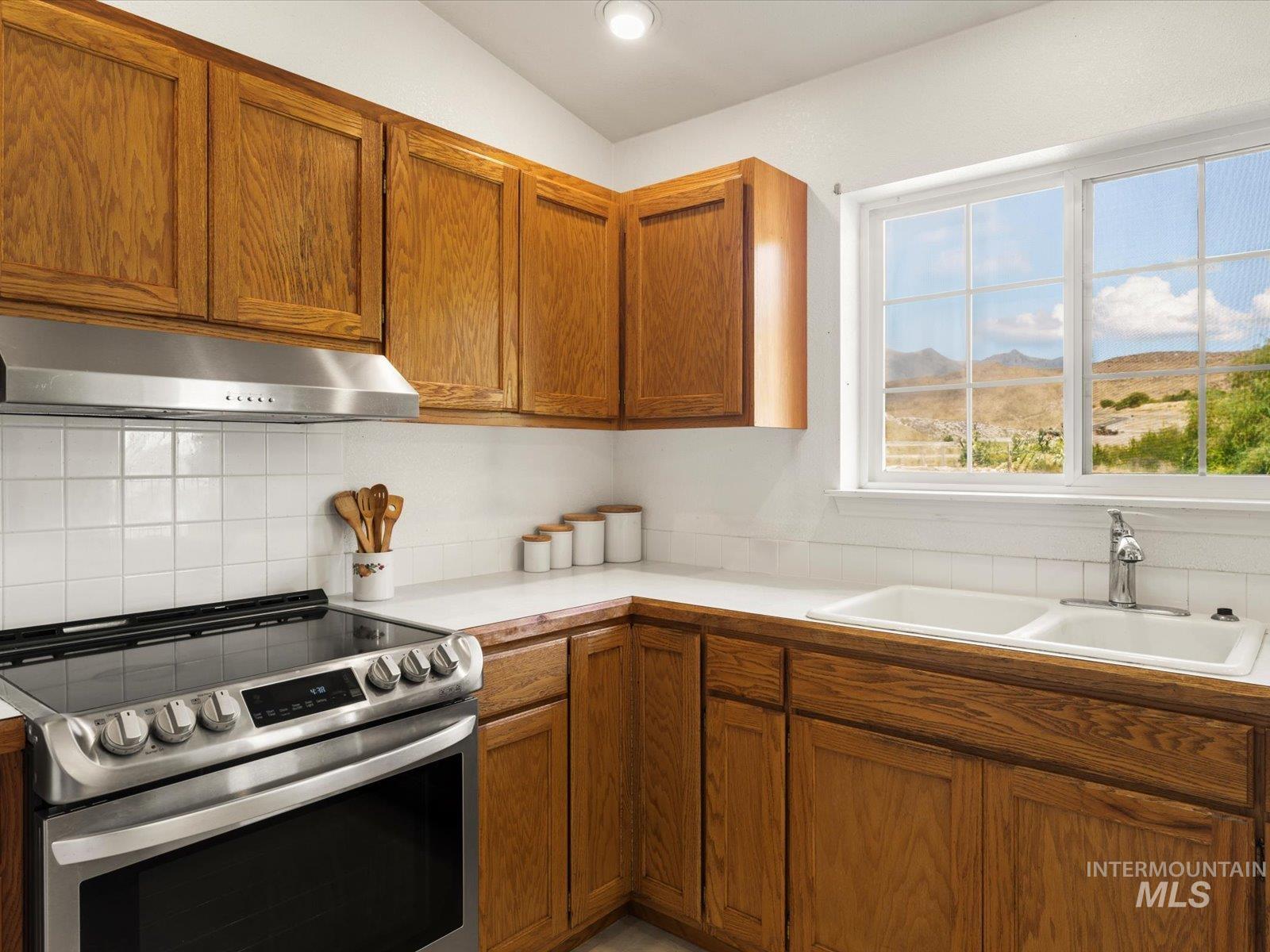 3540 Wills Road Emmett, ID 83617 - Photo 12 of 36 Kitchen featuring wood cabinetry, white square tile backsplash, white countertops, stainless steel range with overhead hood, and a double basin sink