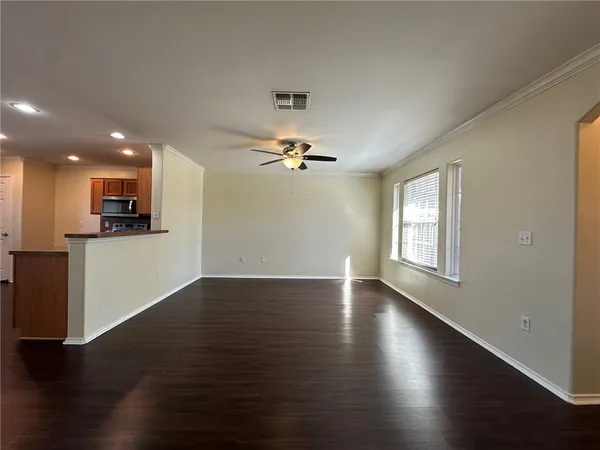 an empty room with wooden floor a ceiling fan and kitchen view