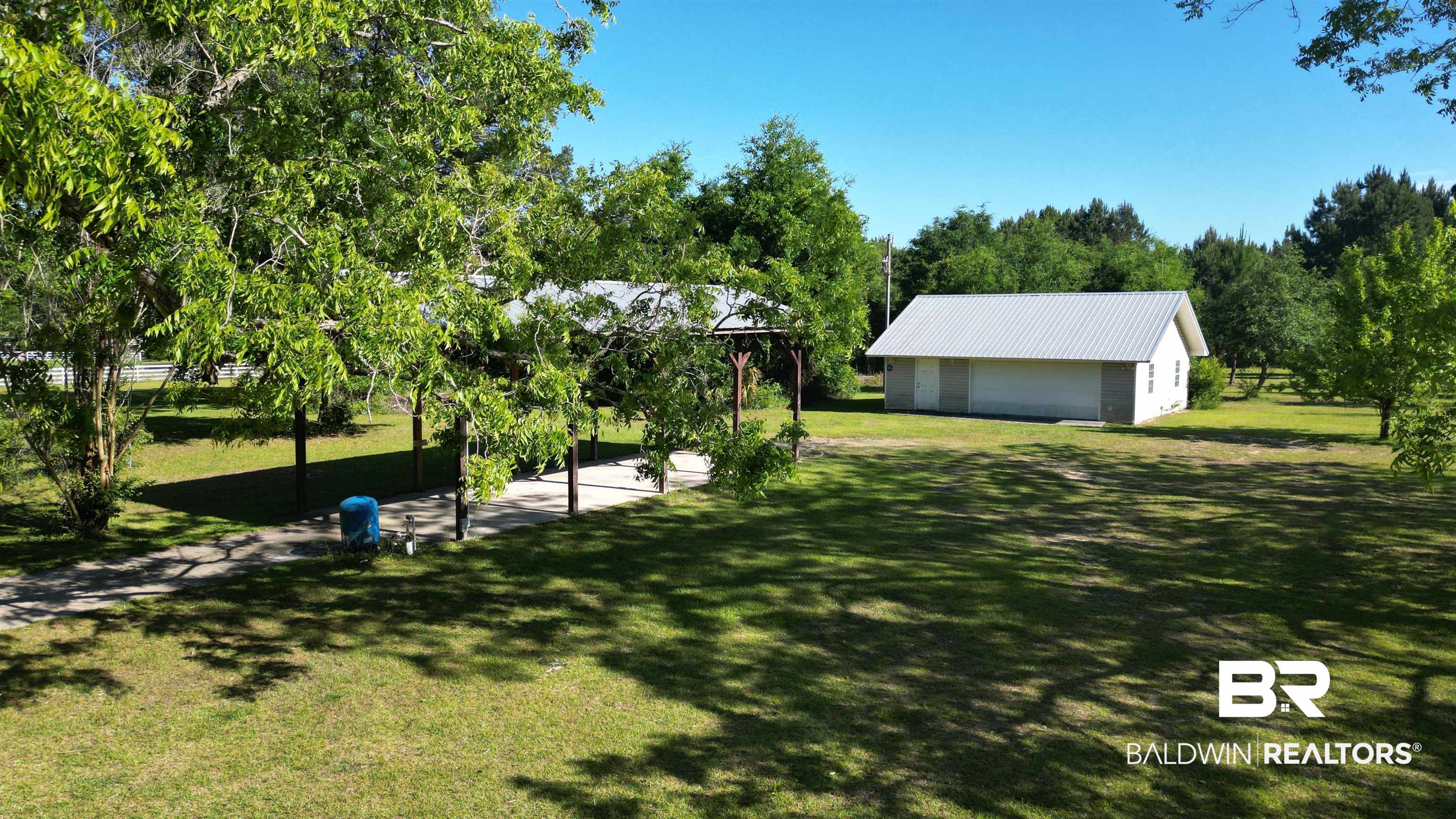 33370 Highway 98 Lillian, AL 36549 - Photo 3 of 58 Spacious property featuring a detached outbuilding with a metal roof, a covered carport, and mature trees providing natural shade