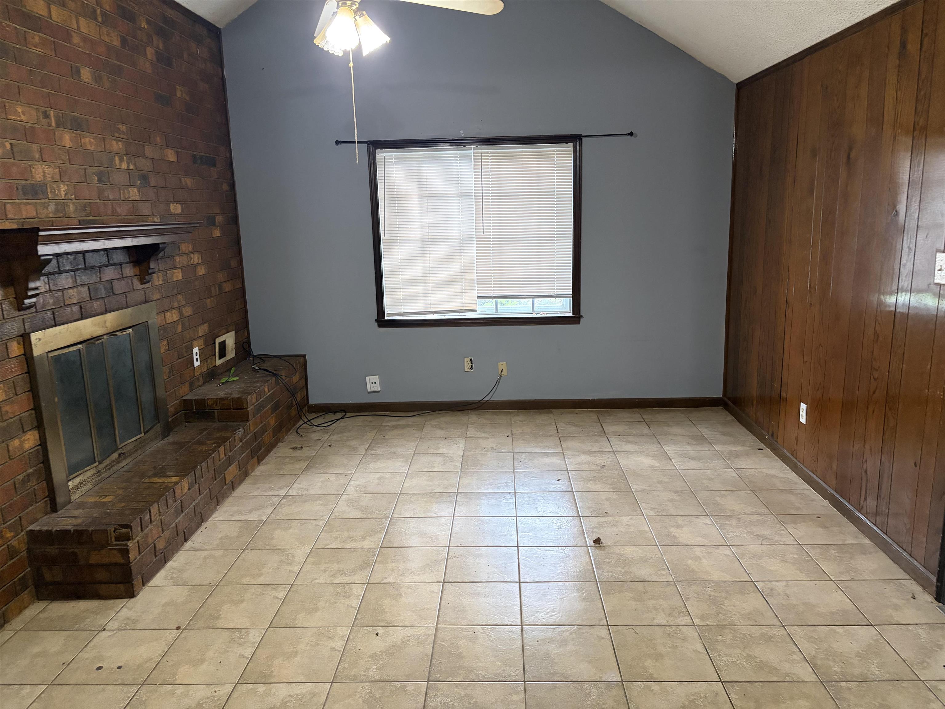 4993 Cedar View Road Memphis, TN 38118 - Photo 18 of 23 Living area featuring a brick fireplace, vaulted ceiling, tile flooring, wood-finish paneling, and a ceiling fan