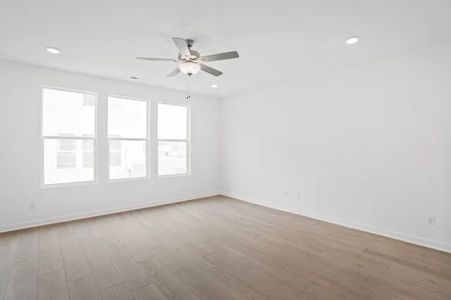 an empty room with wooden floor fan and windows