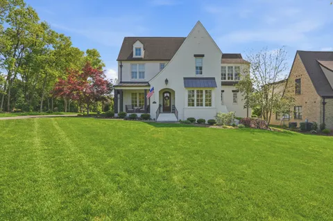 a view of a white house next to a yard with big trees