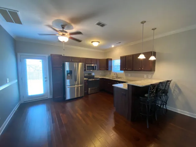 a open kitchen with stainless steel appliances granite countertop a refrigerator a stove a sink dishwasher a dining table and chairs with wooden floor