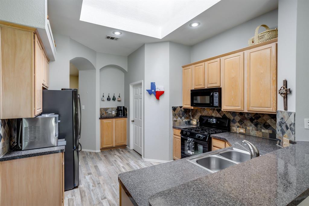 6403 Highland Crest Lane Sachse, TX 75048 - Photo 10 of 40 Kitchen featuring backsplash, black appliances, light brown cabinetry, arched walkways, and light wood finished floors