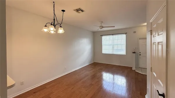an empty room with wooden floor chandelier and windows