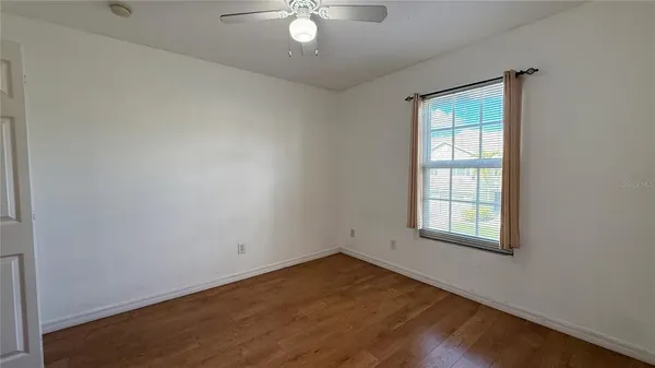 an empty room with wooden floor chandelier fan and windows