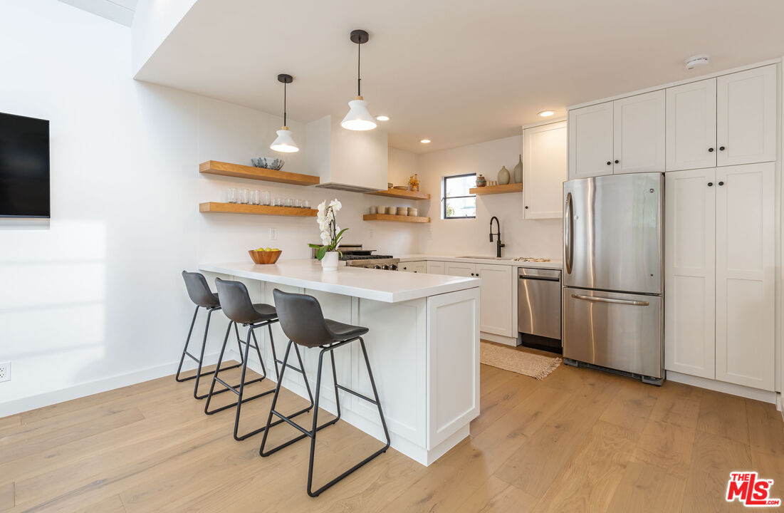 29233 Heathercliff Road, Unit 2 Malibu, CA 90265 - Photo 7 of 20 a kitchen with stainless steel appliances a refrigerator a stove a sink and white cabinets with wooden floor