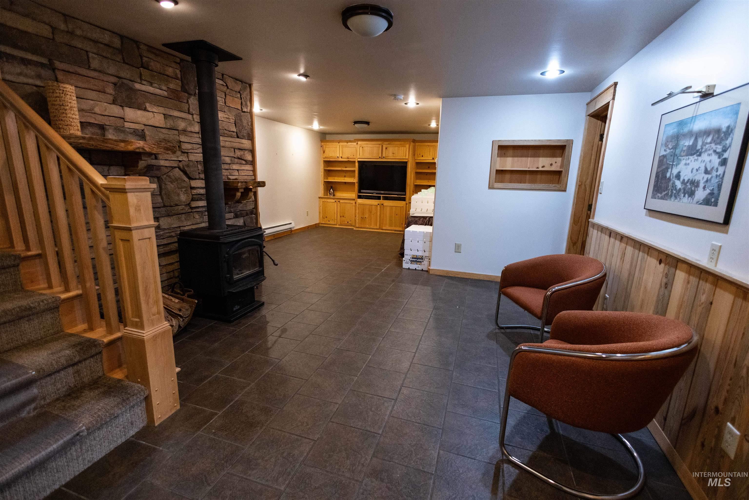 4480 Highway 12 Kamiah, ID 83536 - Photo 39 of 49 Living area with stairs, a wood stove, wood walls, a wainscoted wall, and a baseboard heating unit