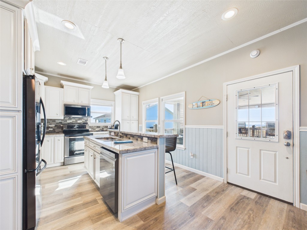 842 Main Street Crystal Beach, TX 77650 - Photo 27 of 45 a kitchen with stainless steel appliances granite countertop a stove top oven a sink a refrigerator and white cabinets with wooden floor