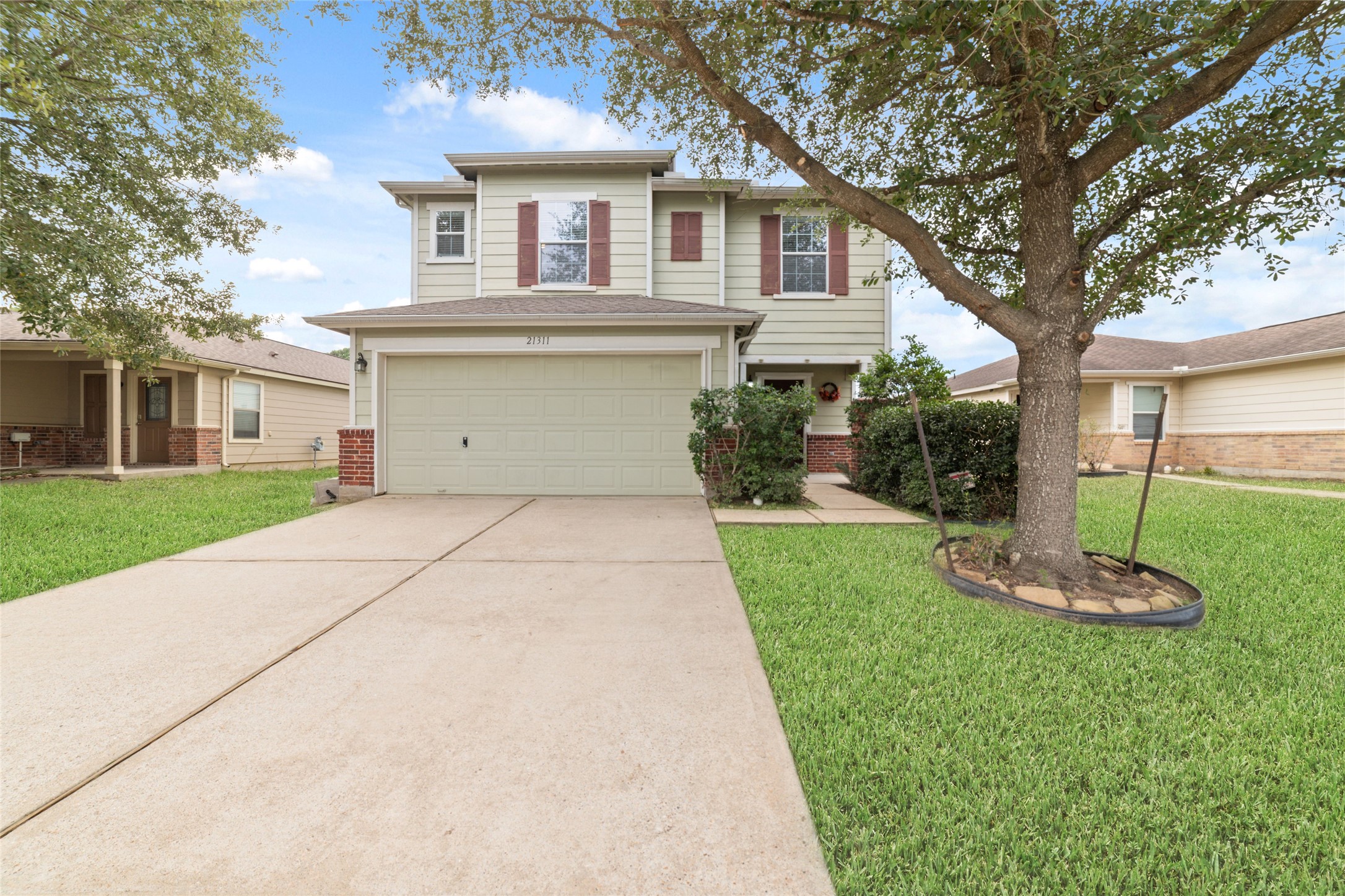 21311 Shadow River Lane Spring, TX 77379 - Photo 8 of 38 This photo shows a two-story suburban home with a two-car garage. The exterior features light siding with brick accents, and there is a well-maintained lawn with a large tree in the front yard. The driveway is spacious, leading to a welcoming entrance.