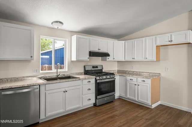 a kitchen with stainless steel appliances granite countertop a sink a stove a refrigerator and white cabinets