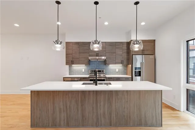 a large kitchen with kitchen island stainless steel appliances a stove a sink and a wooden floor