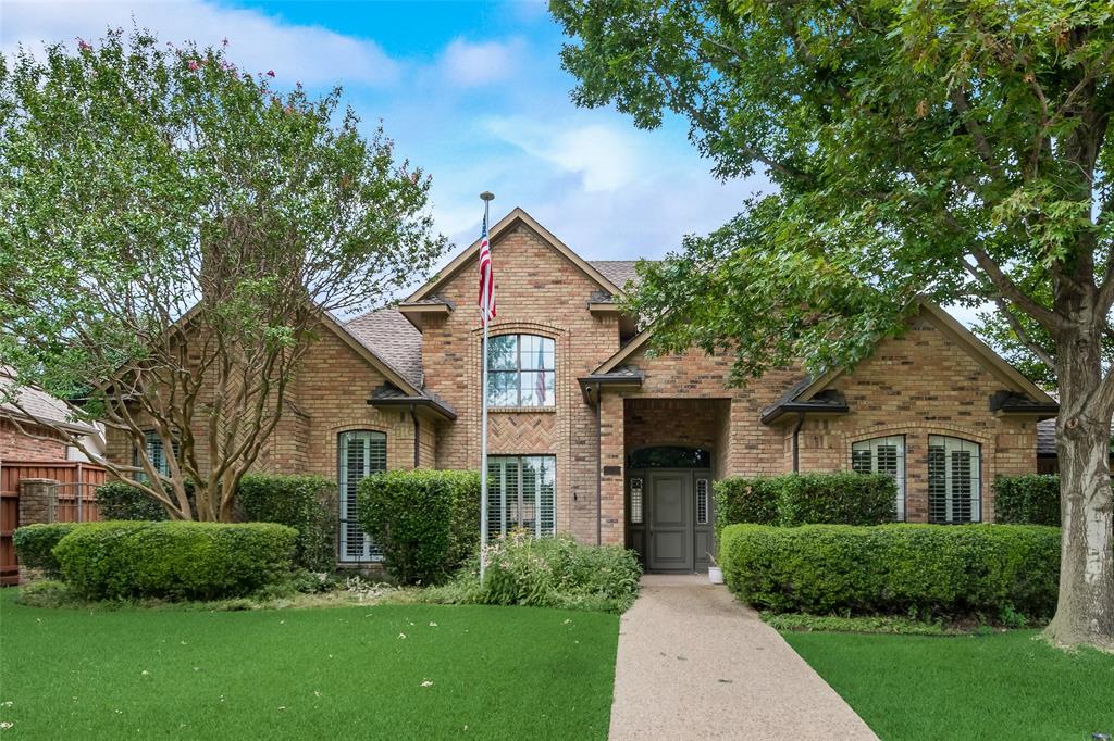 The property features a brick facade, a meticulously maintained lawn, and mature trees providing ample shade