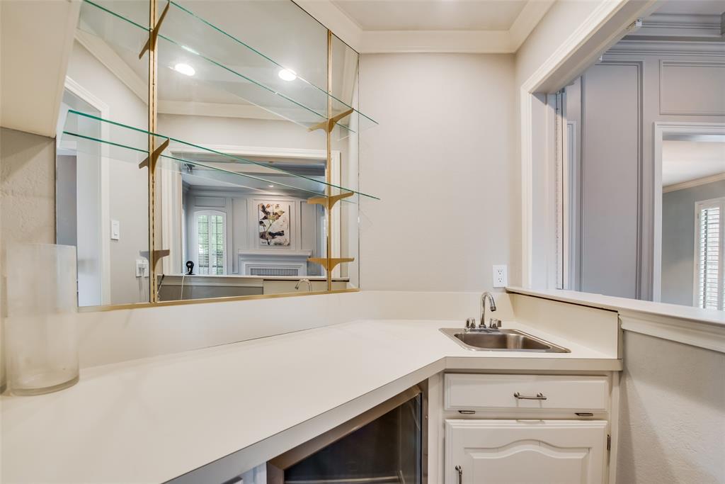 15720 Golden Creek Road Dallas, TX 75248 - Photo 11 of 25 Wet bar area featuring a corner sink with a stainless steel faucet, white cabinetry, and a mirrored backsplash with glass shelving